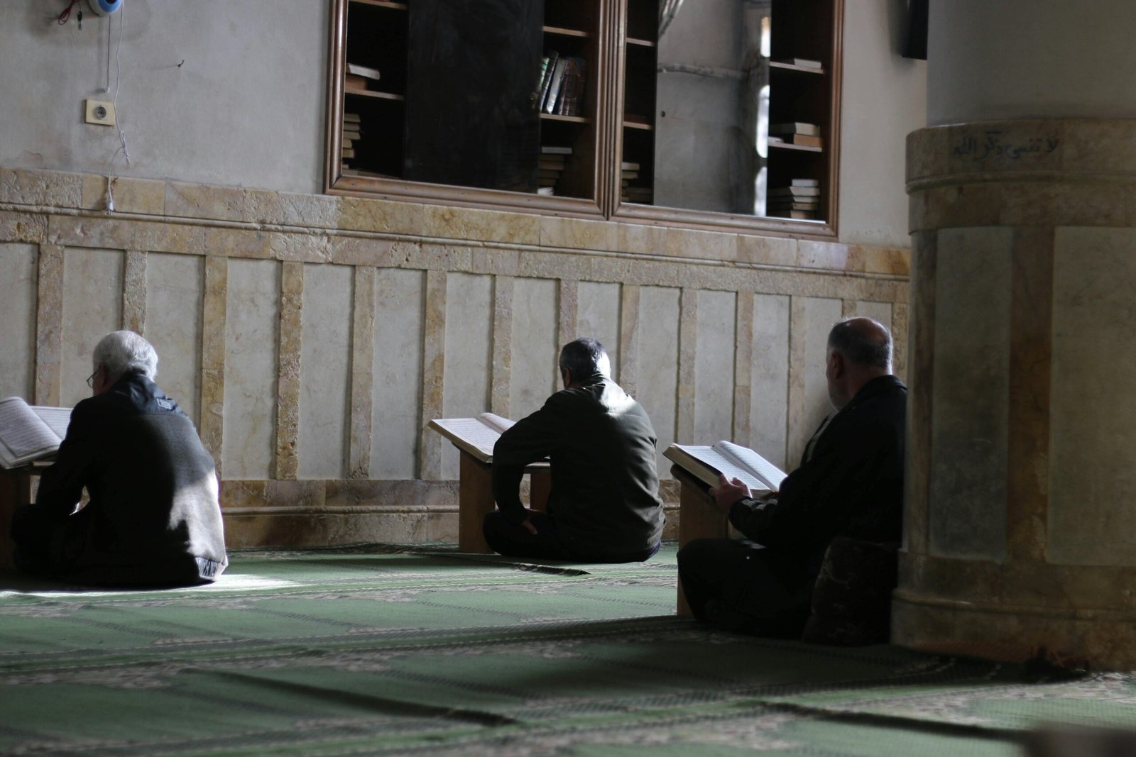 Three men reading Quran and praying inside a mosque in Idlib, Syria.