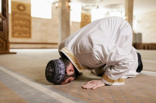 A Muslim man in traditional attire praying inside a mosque, showcasing cultural reverence.