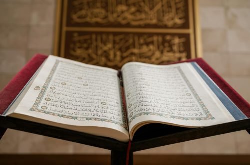 Close-up of an open Quran with ornate pages, featuring Arabic calligraphy in a serene setting.